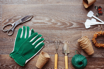Spring gardener table top view with tools, gloves, peat pots and garden labels on brown wooden...