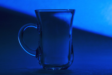 Transparent glass Cup is on a dark background in blue lighting.