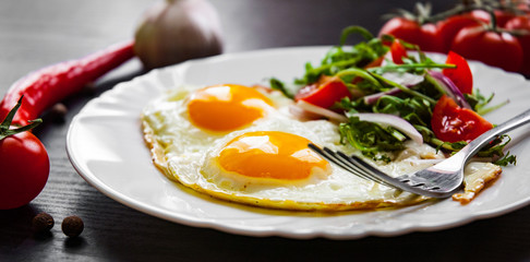 Breakfast. Fresh salad and two fried eggs on dark wooden background