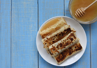  space for text. Pancakes with honey on a blue retro wooden background. Pancakes and honey Maslenitsa. A pile of pancakes, honey, for the celebration of the carnival. Thin pancakes for breakfast.