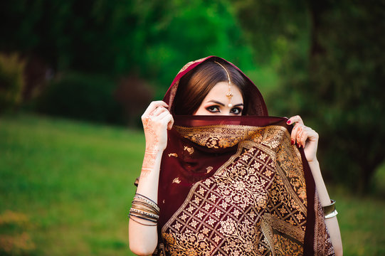 Portrait of beauty Indian model with bright make-up who hiding her face behind the veil. Young Hindu woman with mehndi tattoos from black henna on her hands.