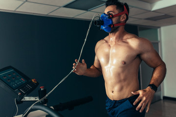 Fit and muscular athlete with mask running on treadmill