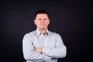 portrait of serious man on black background. Brutal man in a shirt with arms crossed on his chest. An inflated man in a light shirt.