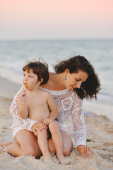 Fototapeta premium mom with baby sitting on the beach and playing sand in summer