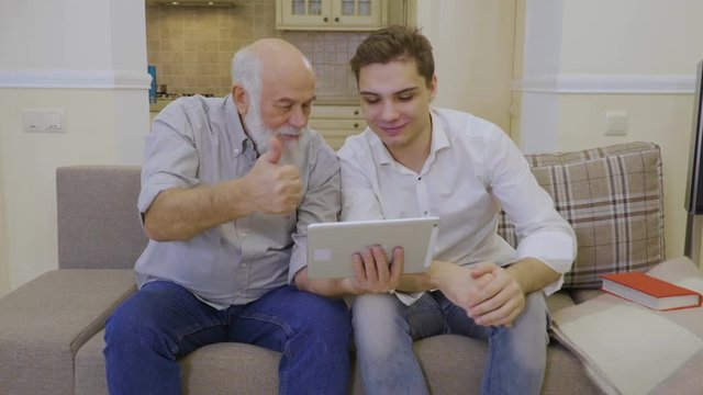 Modern grandfather shows video to his grandson in the internet on digital tablet
