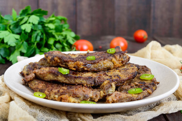 Pieces of fried pork liver on a plate on a dark wooden background.