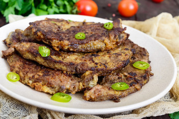 Pieces of fried pork liver on a plate on a dark wooden background.
