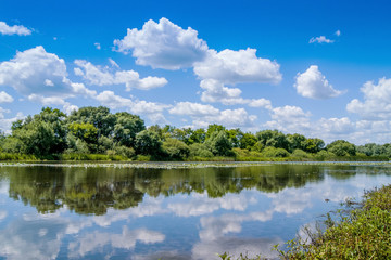 Fototapeta na wymiar summer landscape: a river in which white curly clouds are displayed