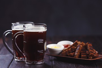Two mugs of stout and crunchy rye toasts, served with tomato and cheese sauces, close up. Oktoberfest food, dark beer and appetizing beer snacks, pub concept