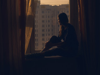 Profile Shot Of Sad Woman Sitting On Window Sill at Sunset Time on the Background of a Panel Building