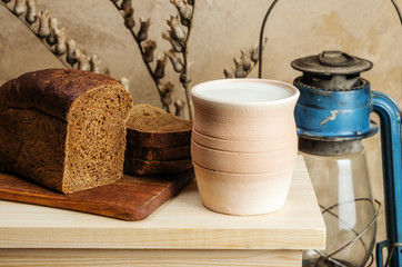 Milk in a clay pot and rye bread. Still-life in the rustic style