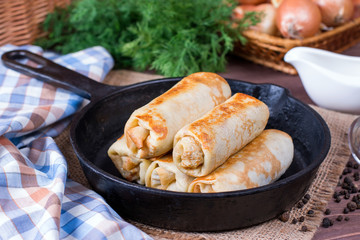 Crepes stuffed with minced meat and rice in a frying pan on a wooden table