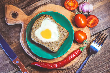 fried bread. fried eggs in a heart-shaped symbol. vegetables. on a wooden board