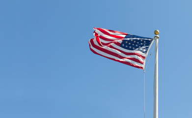 The United States flag on blue sky bacground, turned to the left