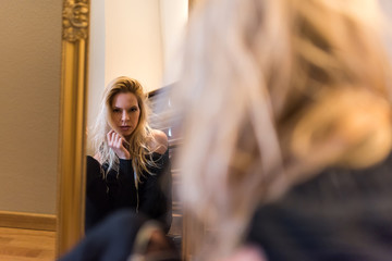 A beautiful young woman sitting on the floor and looking at herself in the mirror and wearing black clothes.