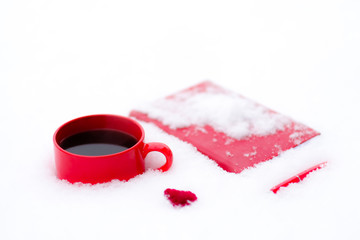Red cup of coffee or tea with a red book or notebook or photo albums with heart. Snow is coming. Winter concept of Valentine's Day