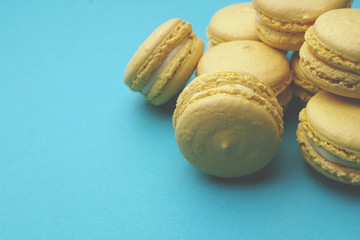 Stack of yellow macaroons on blue background. Colorful almond cookies. Pastel cake macarons background. Place for text. Toned image