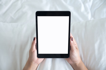 Top view mockup image of a woman holding black tablet pc with blank desktop white screen while sitting on a white bed background
