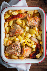 Baked potatoes with sausages and chicken in enameled form, top view