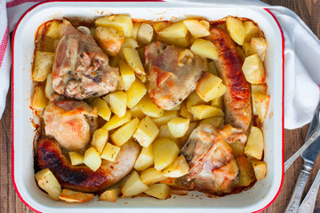 Baked potatoes with sausages and chicken in enameled form on a wooden table, top view, horizontal
