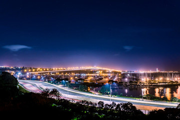 cars in motion on a lighted bridge and highway over the sea with anchored sailing boats in a marina...