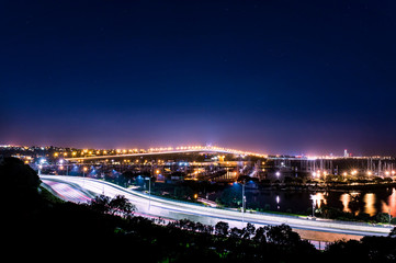 cars in motion on a lighted bridge and highway over the sea with anchored sailing boats in a marina of Auckland in New Zealand with a Starry sky