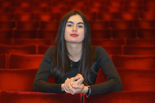 Brunette Young Woman Sitting In The Empty Red Theater Hall