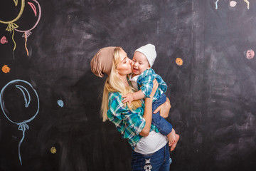 A modern mom hipster is holding a child's kiss and hugs him on a black background. Young beautiful...