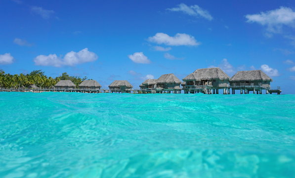 Over water bungalows with thatched roof in a tropical lagoon, seen from sea surface, Tikehau atoll, Tuamotus, French Polynesia, Pacific ocean, Oceania