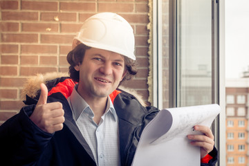 A construction worker giving his thumbs-up in front of a newly constructed residential building. Soft focus, toned.