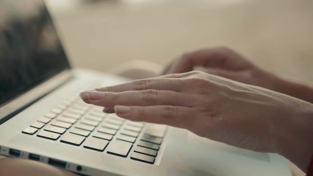 A close up of the workplace on the beach. Young lady is looking for a job in the Internet using the laptop. A concept of freelance ICO from asia hands.