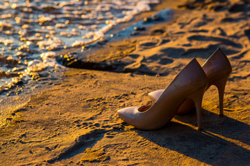 Nude bride's shoes on the sand beach near the water