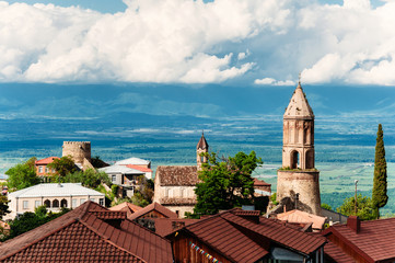Fototapeta premium Old houses with brown tile roofs, church of St. George in city of love - Sighnaghi, Kakheti, Georgia. Beautiful view on Alazani valley. Sunny day with blue sky with clouds.