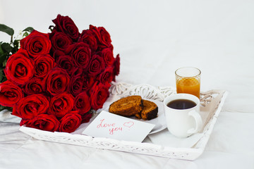 Breakfast in bed, celebrate valentines day, womens day or birthday. White bed, large bouquet of red roses. In the background of a pillow, a bedside table unfocus. copy space, free space.