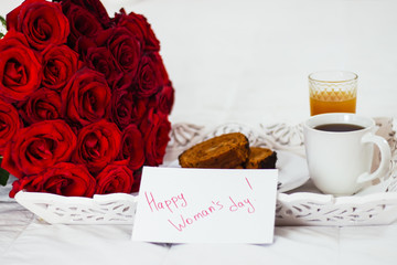 Breakfast in bed, celebrate valentines day, womens day or birthday. White bed, large bouquet of red roses. In the background of a pillow, a bedside table unfocus. copy space, free space.