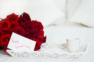 Breakfast in bed, celebrate valentines day, womens day or birthday. White bed, large bouquet of red roses. In the background of a pillow, a bedside table unfocus. copy space, free space.