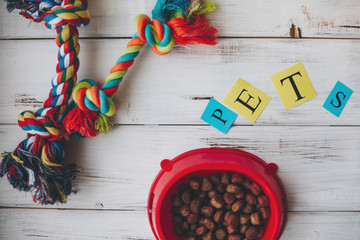 A bowl of dry dog food and rope toy on a white board background. Pet care and veterinary concept. Top view