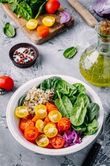 Healthy green bowl salad with spinach, quinoa, yellow and red tomatoes, onions and seeds