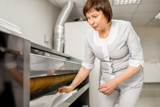 Senior woman in unifrom working with professional ironing machine in the laundry
