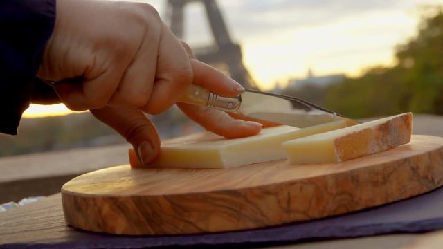 Hands are stabbing a piece of Parmesan cheese on a wooden board close-up on a background of the Eiffel Tower