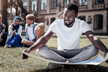 Future engineer. Joyful positive smart student sitting on the grass and studying a drawing while...