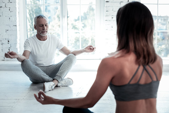 In a good mood. Selective focus on a senior gentleman in sportswear sitting on a mat with a slight smile on his face while attending a yoga class and meditating.