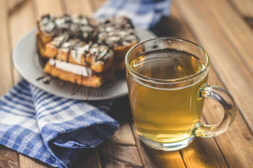 waffles with cream and chocolate on the plate and green tea on a wooden table.