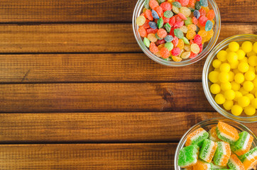 Brightly colored candies in glass cups on a wooden table, top view, free space for text