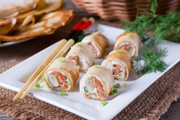 Tasty roll of pancakes with fish and cream cheese on plate