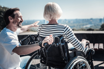 Amazing view. Happy positive cheerful man smiling to an elderly woman and pointing with his hand while showing her the view