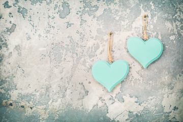 Two handmade Valentine's day love hearts hanging on vintage aged grunge textured concrete wall background. Retro old style filtered photo