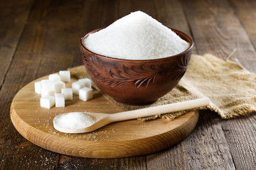   Bowl and spoon full of sugar on wooden background