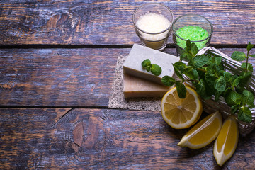 Spa setting with slice of lemon and mint on a table, nature soap, parfume salt on the wooden background