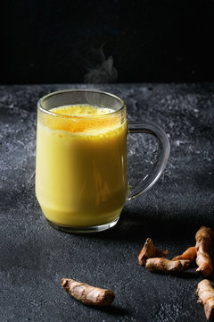 Cup of ayurvedic drink golden milk turmeric latte with curcuma powder and ingredients above over black texture background.